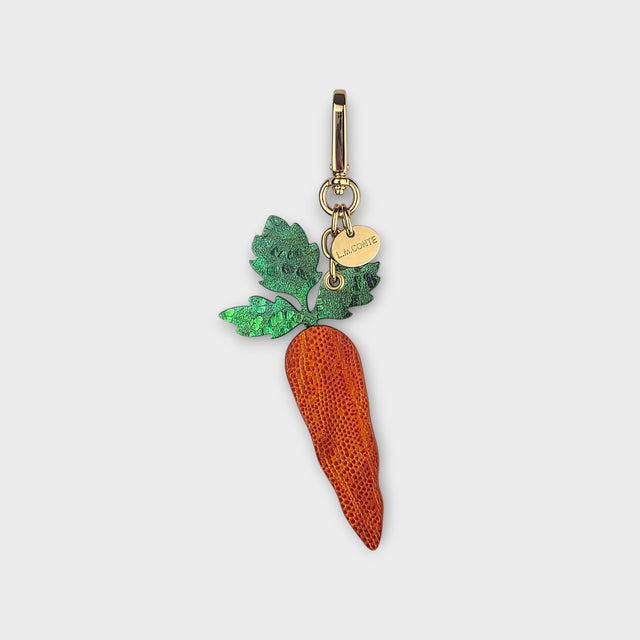 Carrot-shaped bag charm with green leaves at the top and orange body on a light gray background.