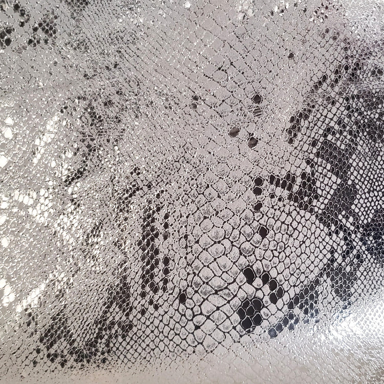 Close-up of a scale pattern of foiled silver metallic embossed on a soft gray lambskin leather.
