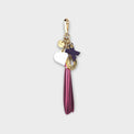Handbag fringe tassel with X-O letters and heart charm linked on gold tone hardware against a light gray background.