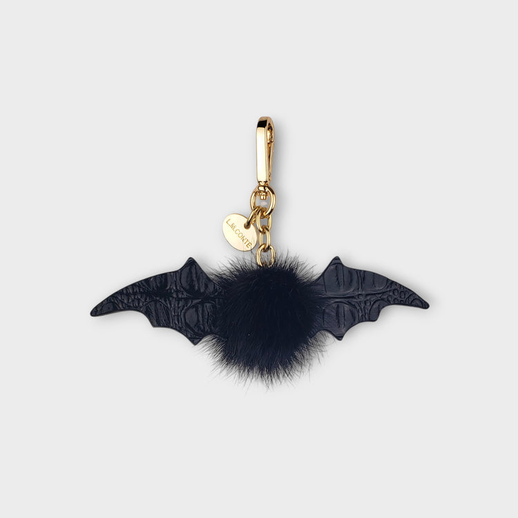 Bat-shaped keychain with a black mink fur pom-pom on a light gray background
