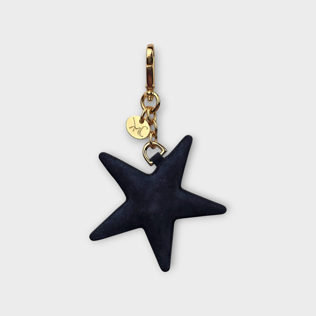 A dark navy blue suede celestial star charm with gold-tone hardware, featuring a small gold tag engraved with 'LMC'.