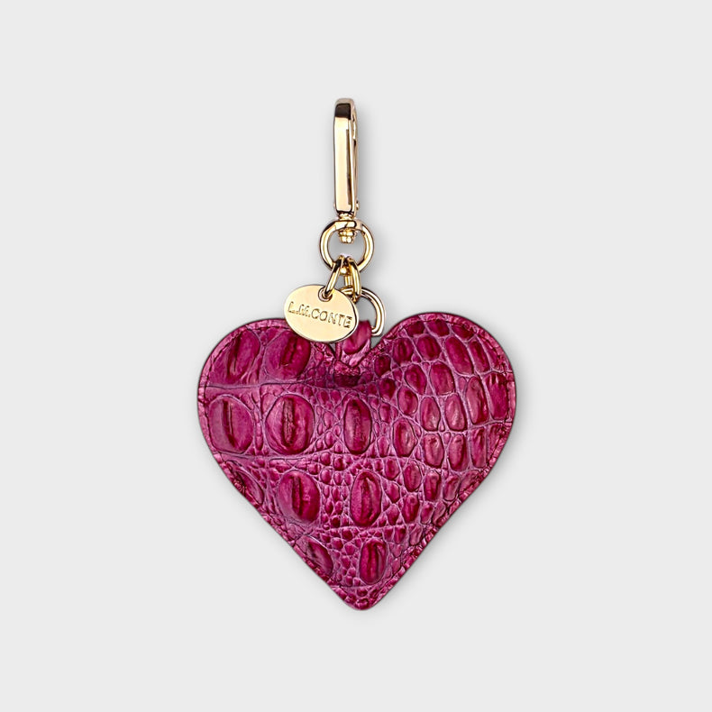 Pink heart-shaped bag charm with gold hardware on a light gray background.