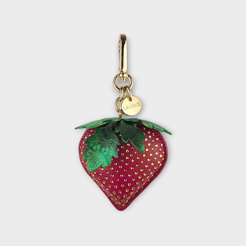 Strawberry-shaped handbag charm with gold hardware on a light gray background.