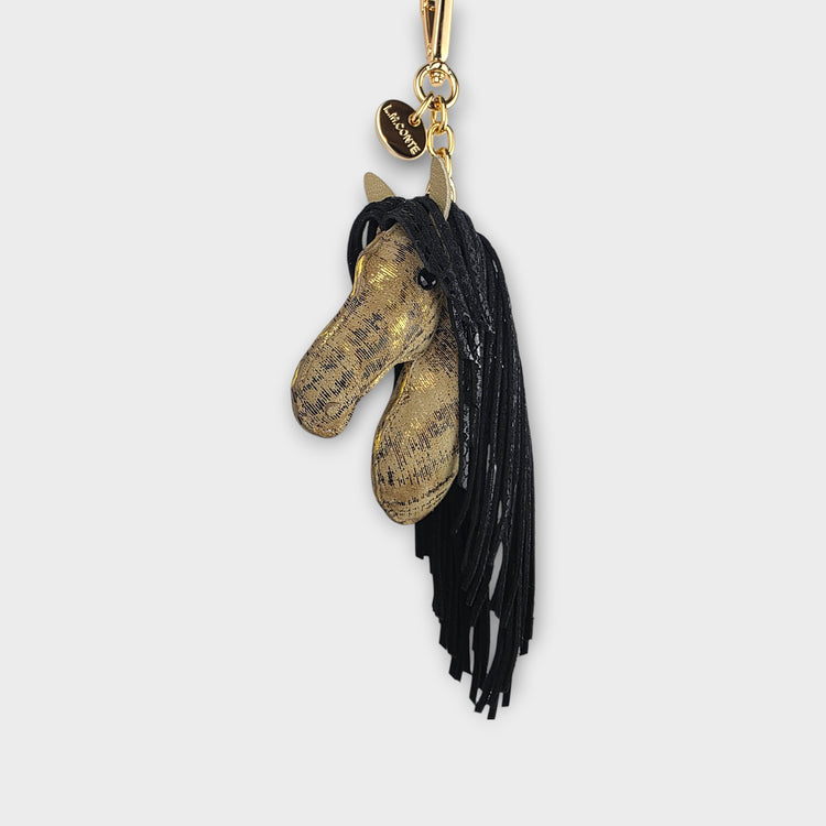Gold and tan horse head keychain with black fringe as the mane against a gray background.